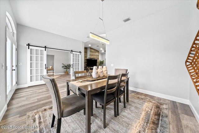 dining space with a barn door, vaulted ceiling, and hardwood / wood-style flooring