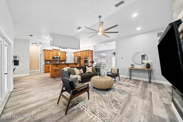 living room with ceiling fan, light hardwood / wood-style floors, a textured ceiling, and vaulted ceiling