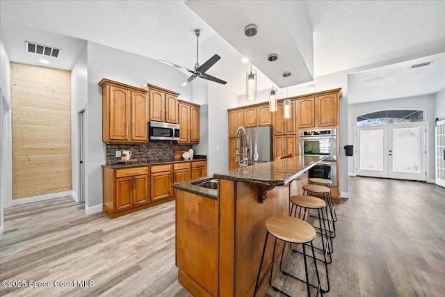 kitchen featuring sink, an island with sink, a kitchen bar, decorative backsplash, and appliances with stainless steel finishes