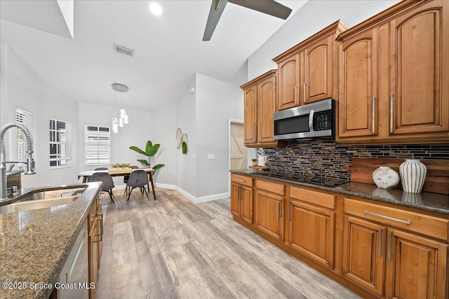 kitchen featuring appliances with stainless steel finishes, light wood-type flooring, dark stone counters, sink, and decorative light fixtures