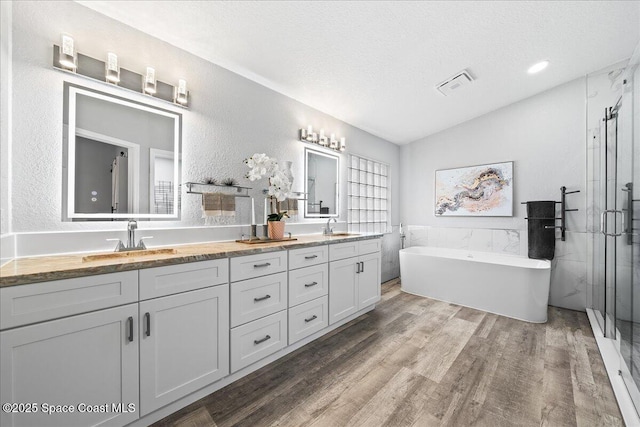 bathroom featuring plus walk in shower, wood-type flooring, lofted ceiling, a textured ceiling, and vanity