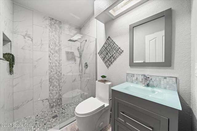 bathroom with vanity, a skylight, decorative backsplash, toilet, and tiled shower