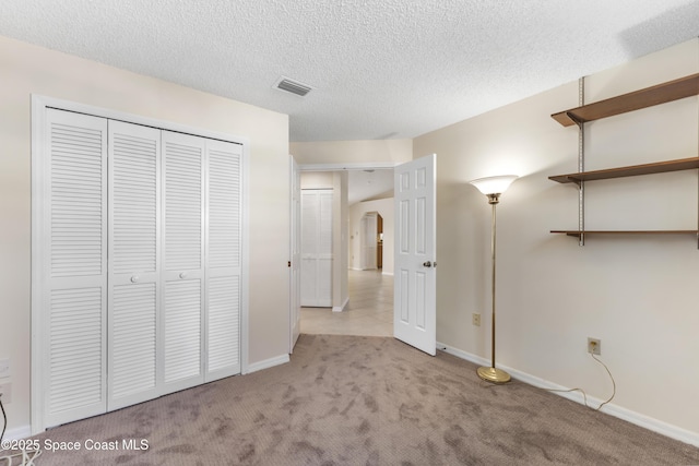 unfurnished bedroom with light carpet, a textured ceiling, and a closet