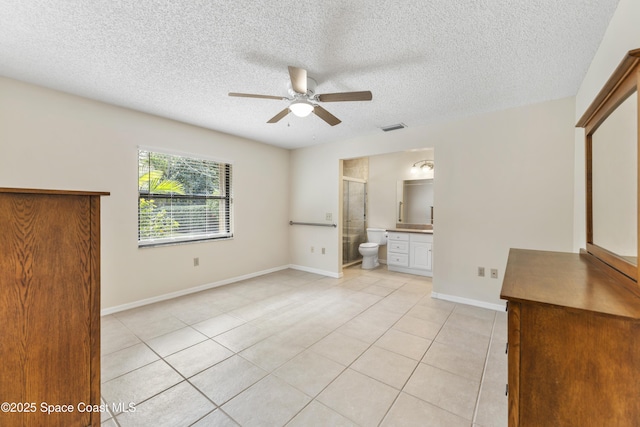 unfurnished bedroom featuring ceiling fan, ensuite bathroom, a textured ceiling, and light tile patterned floors