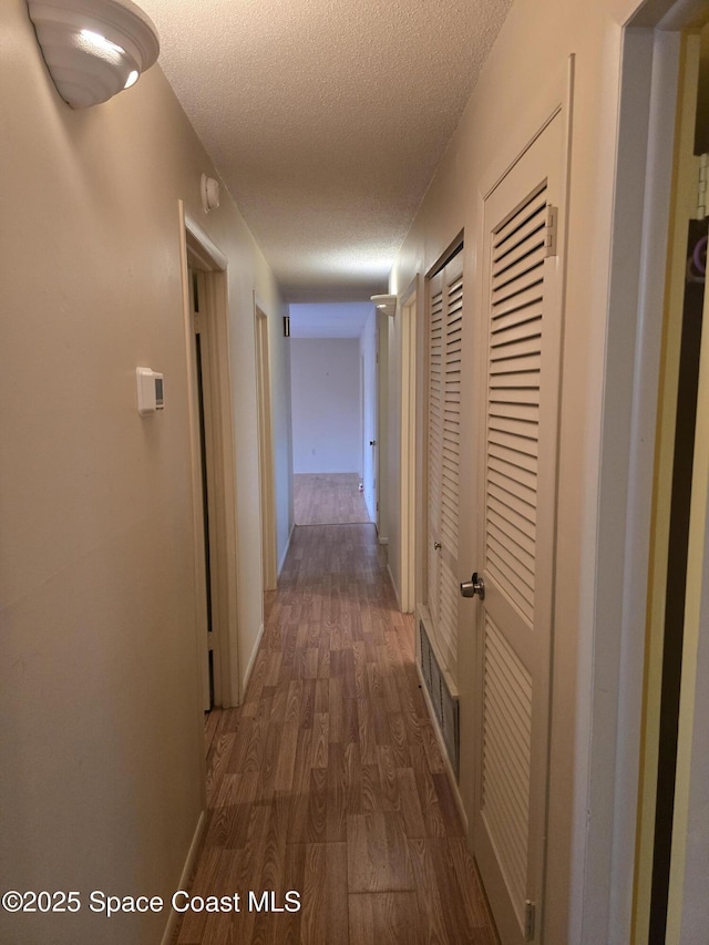 corridor with a textured ceiling and dark hardwood / wood-style floors