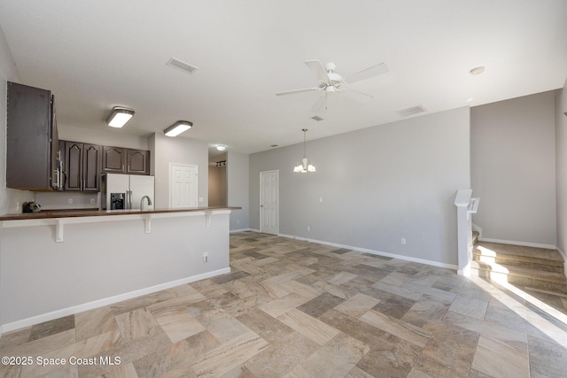 kitchen featuring stainless steel fridge, a breakfast bar, dark brown cabinetry, ceiling fan with notable chandelier, and kitchen peninsula