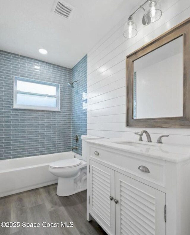 full bathroom featuring vanity, wood-type flooring, tiled shower / bath combo, and toilet