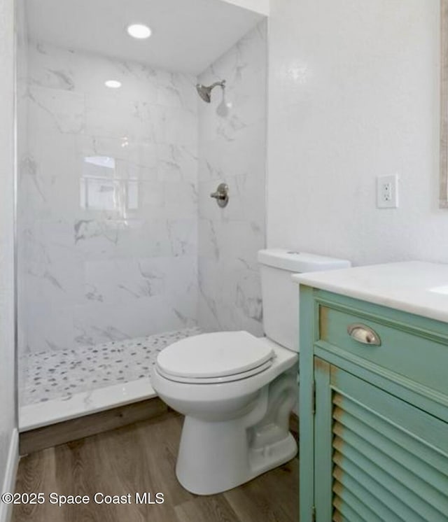 bathroom with tiled shower, toilet, vanity, and hardwood / wood-style flooring