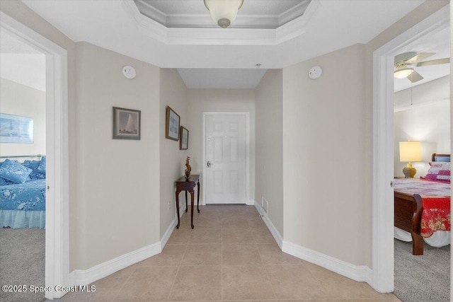 corridor featuring crown molding, a tray ceiling, and light tile patterned floors