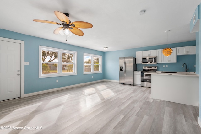 kitchen featuring appliances with stainless steel finishes, light wood-type flooring, ceiling fan, white cabinets, and hanging light fixtures