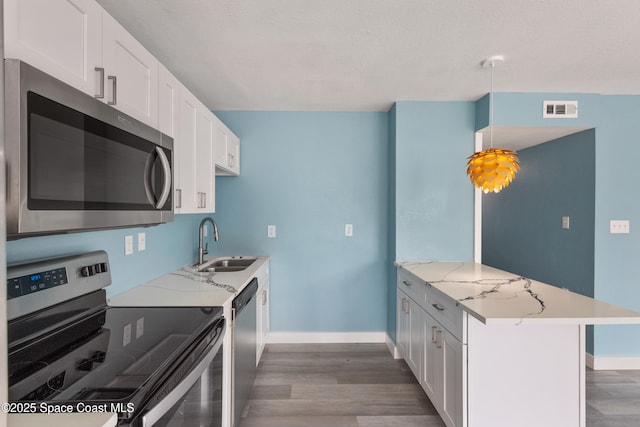 kitchen featuring appliances with stainless steel finishes, light stone counters, sink, decorative light fixtures, and white cabinetry