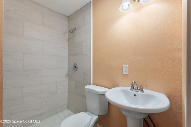 bathroom with a tile shower, toilet, and sink