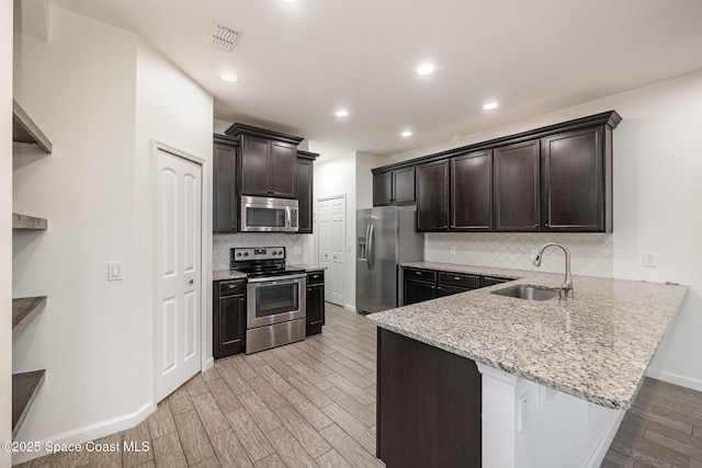 kitchen featuring light stone countertops, sink, stainless steel appliances, kitchen peninsula, and light wood-type flooring