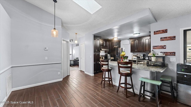 kitchen featuring light stone countertops, stainless steel refrigerator with ice dispenser, pendant lighting, a breakfast bar, and dark brown cabinets