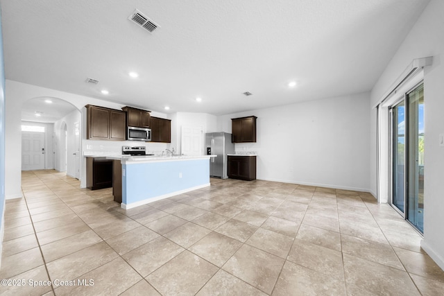 kitchen with a kitchen island with sink, sink, appliances with stainless steel finishes, dark brown cabinets, and light tile patterned flooring