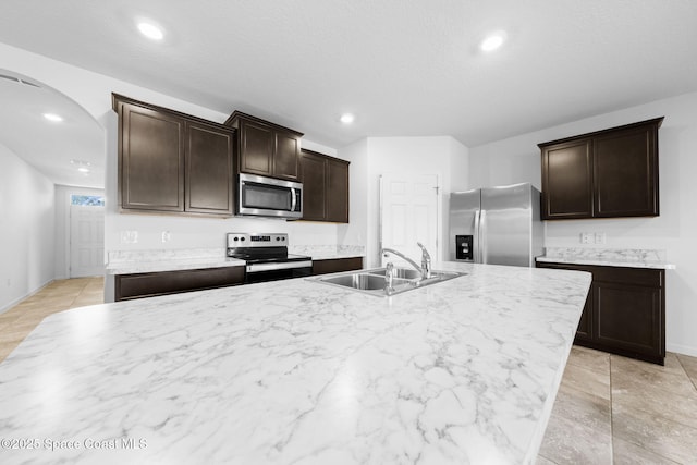 kitchen featuring dark brown cabinets, sink, stainless steel appliances, and an island with sink