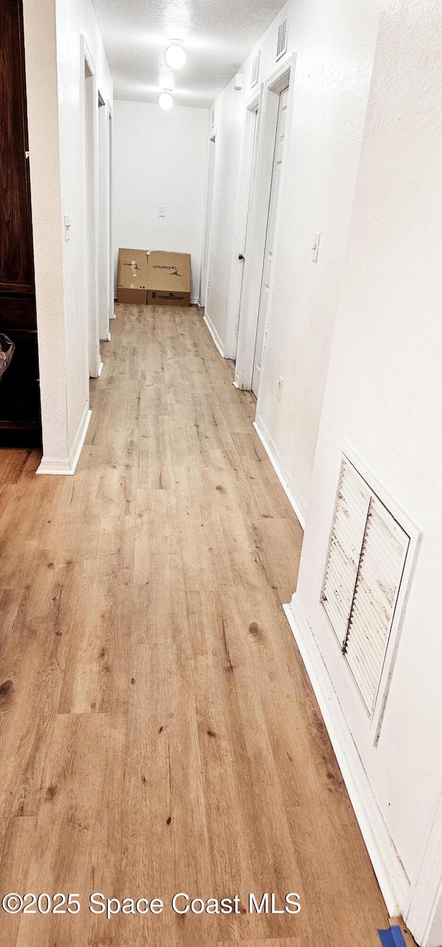 corridor with light hardwood / wood-style floors and a textured ceiling