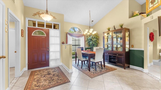 foyer entrance featuring light tile patterned floors, high vaulted ceiling, a textured ceiling, and an inviting chandelier