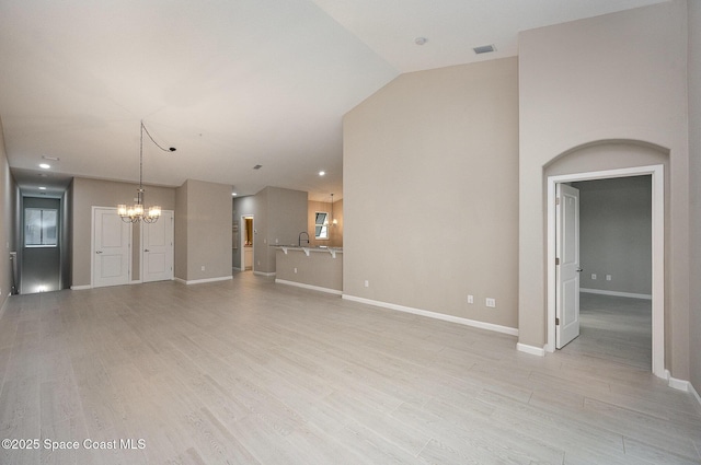 unfurnished living room with a notable chandelier, light hardwood / wood-style floors, sink, and vaulted ceiling