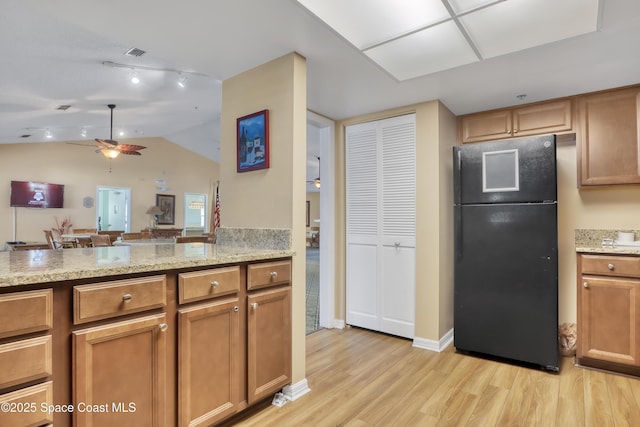 kitchen with light stone countertops, light wood-type flooring, black fridge, and ceiling fan