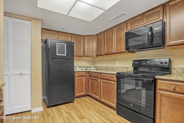 kitchen featuring black appliances, light hardwood / wood-style floors, and light stone countertops