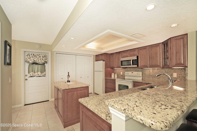 kitchen featuring light stone countertops, a center island, kitchen peninsula, white appliances, and a tray ceiling