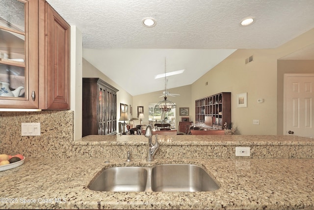 kitchen featuring decorative backsplash, light stone counters, lofted ceiling, and sink