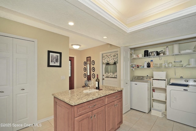 kitchen with light stone counters, ornamental molding, separate washer and dryer, a center island, and light tile patterned flooring