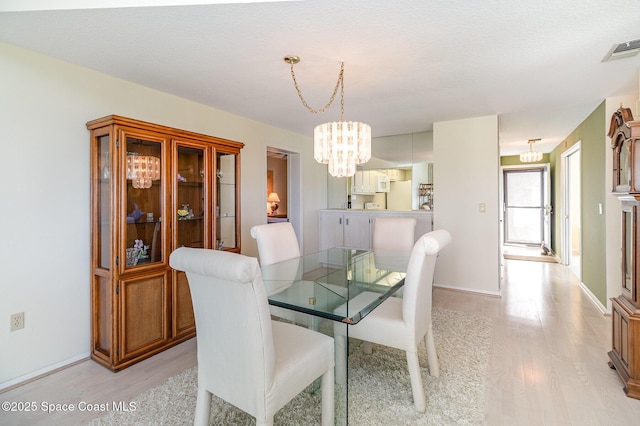 dining room featuring light wood-type flooring, an inviting chandelier, baseboards, and visible vents