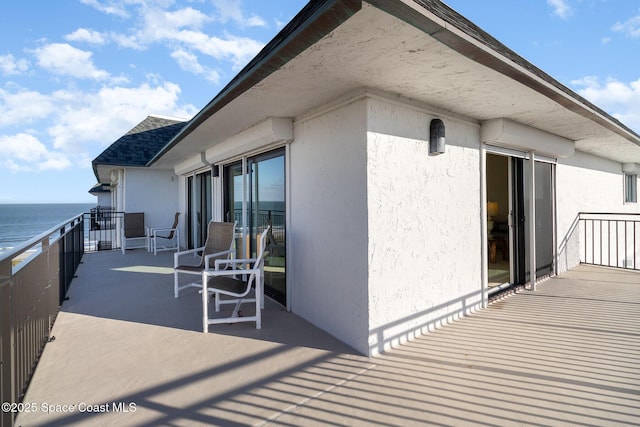 exterior space featuring a water view, roof with shingles, a balcony, and stucco siding