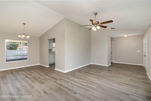 empty room with a textured ceiling, hardwood / wood-style floors, ceiling fan with notable chandelier, and lofted ceiling