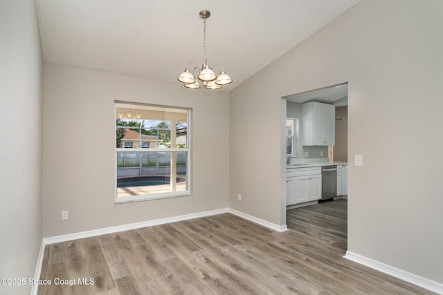 spare room featuring lofted ceiling, sink, a textured ceiling, light hardwood / wood-style floors, and a chandelier