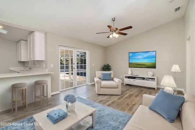 living room with ceiling fan, french doors, sink, lofted ceiling, and light wood-type flooring