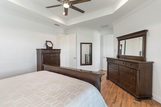 bedroom with ceiling fan, light hardwood / wood-style floors, a raised ceiling, and crown molding