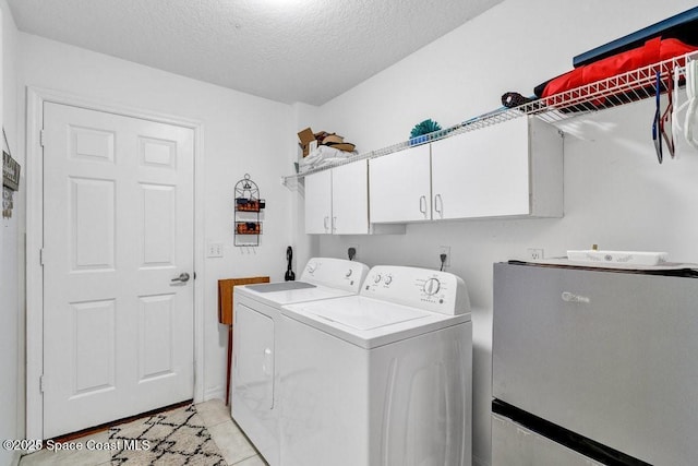 clothes washing area featuring cabinets, light tile patterned floors, a textured ceiling, and washing machine and dryer