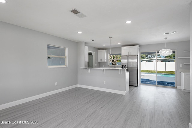 kitchen featuring white cabinetry, hanging light fixtures, light hardwood / wood-style flooring, stainless steel refrigerator with ice dispenser, and a kitchen bar