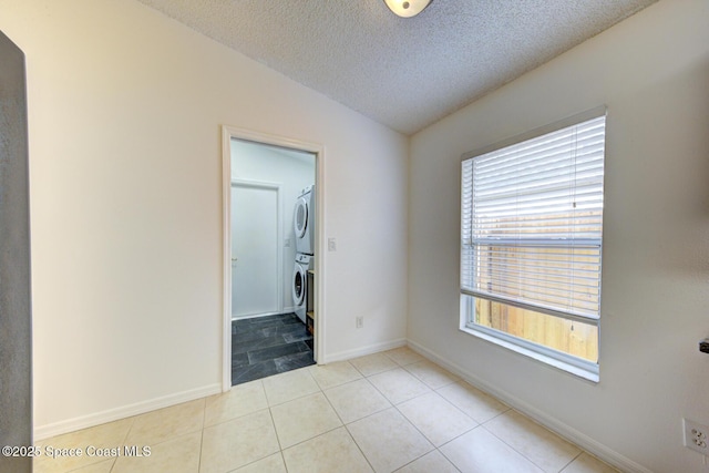 unfurnished room with stacked washer / drying machine, light tile patterned flooring, a textured ceiling, and vaulted ceiling