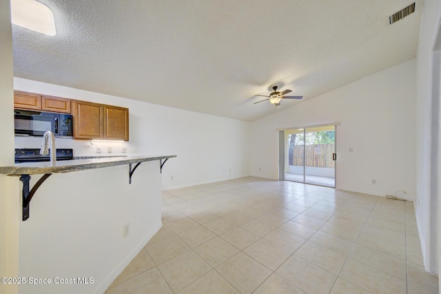 kitchen featuring a breakfast bar, vaulted ceiling, ceiling fan, black appliances, and light tile patterned floors