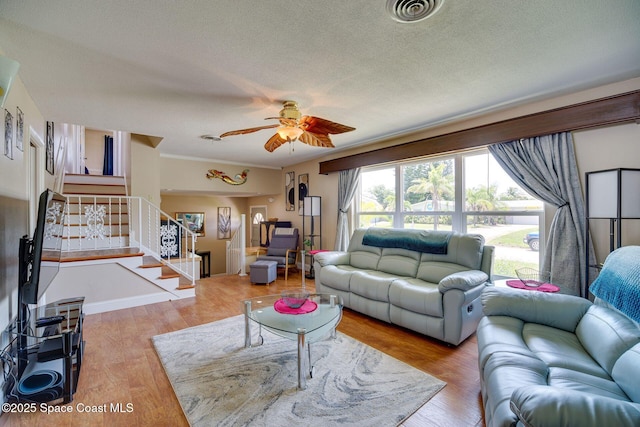 living room featuring a textured ceiling, light wood-type flooring, ceiling fan, and ornamental molding