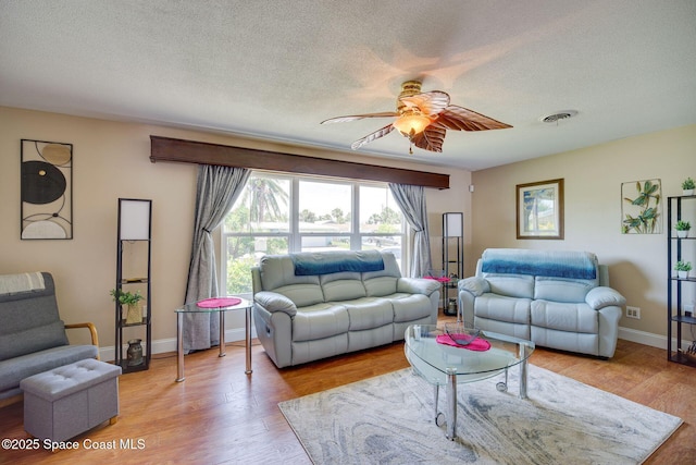 living room with ceiling fan, light wood-type flooring, and a textured ceiling