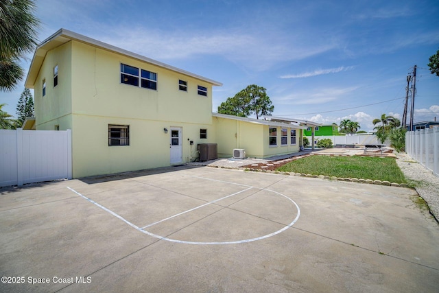 rear view of house with a patio, basketball court, central AC unit, and a lawn