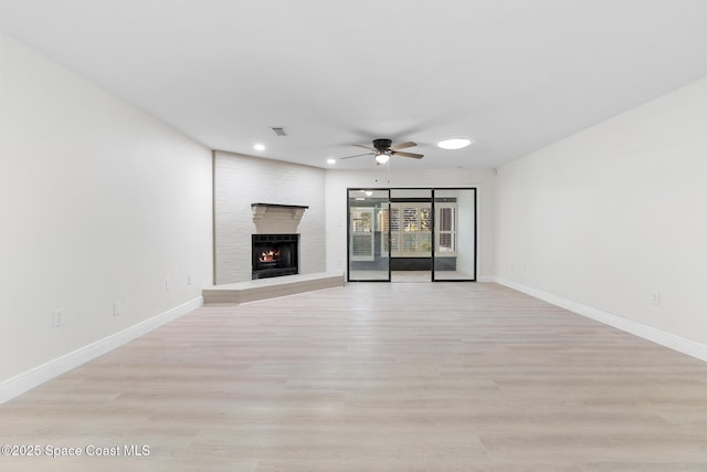 unfurnished living room featuring ceiling fan, a large fireplace, and light wood-type flooring