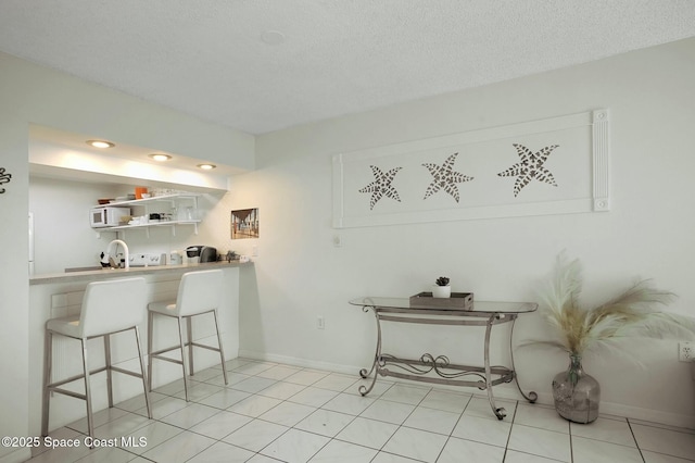 interior space featuring light tile patterned flooring, a textured ceiling, a breakfast bar area, and sink