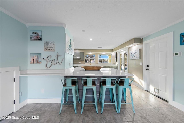 kitchen with a breakfast bar area, ornamental molding, light tile patterned floors, kitchen peninsula, and a textured ceiling