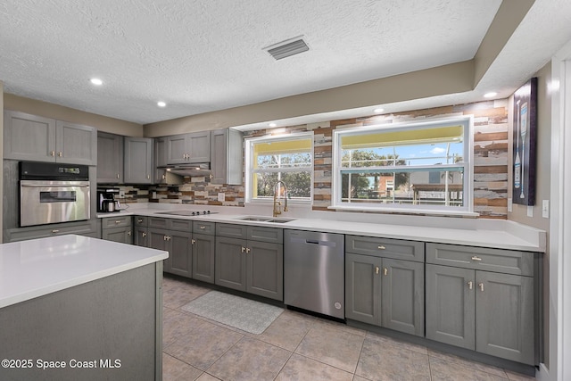 kitchen with sink, gray cabinetry, decorative backsplash, stainless steel appliances, and a textured ceiling