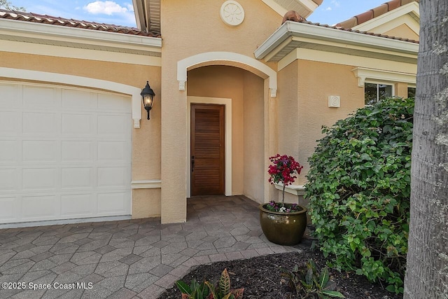 view of exterior entry featuring stucco siding, an attached garage, and a tile roof