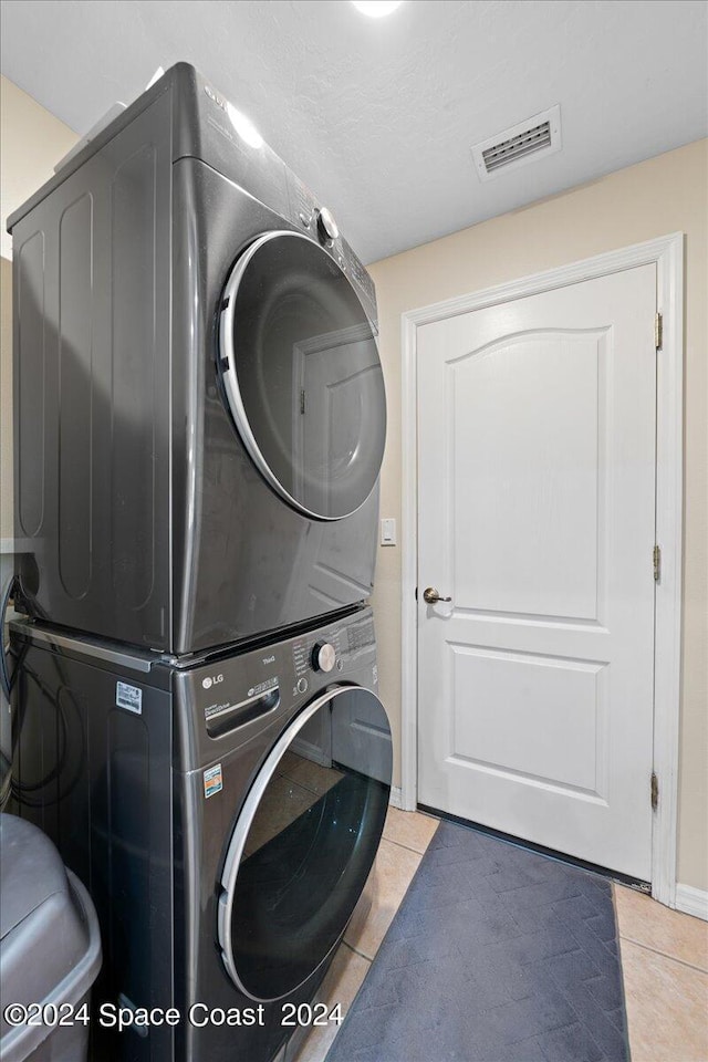 clothes washing area with tile patterned floors and stacked washer / drying machine