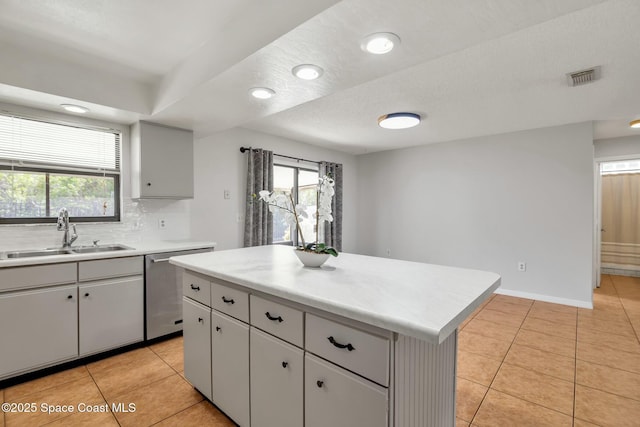 kitchen featuring sink, light tile patterned floors, backsplash, a kitchen island, and stainless steel dishwasher