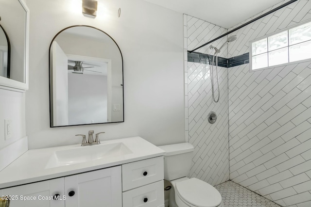 bathroom with a tile shower, vanity, toilet, and ceiling fan