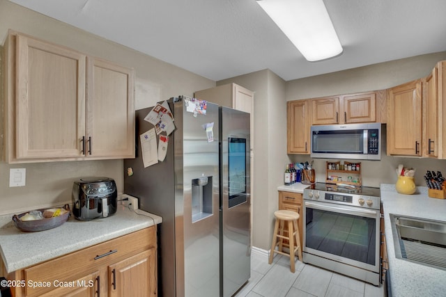 kitchen with light brown cabinets, light tile patterned floors, and stainless steel appliances